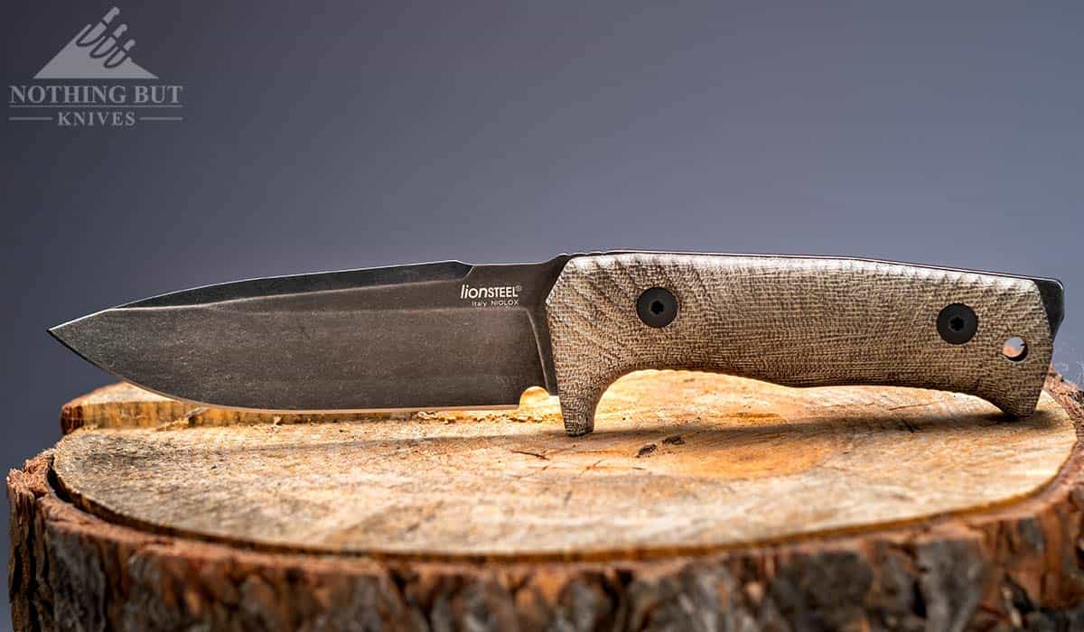 The LionSteel T5 Survival Knife sitting on a piece of firewood with the point of its blade pointing to the left.