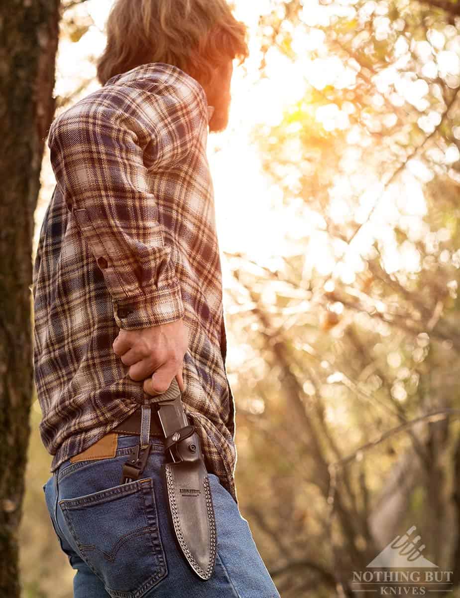 A man in a forest drawing the LionSteel T5 knife from it's leather sheath. 