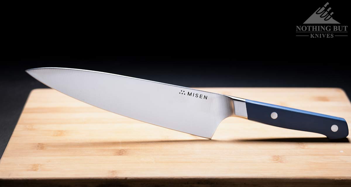 The Misen 8 inch chef knife with a blue handle on a wooden cutting board.