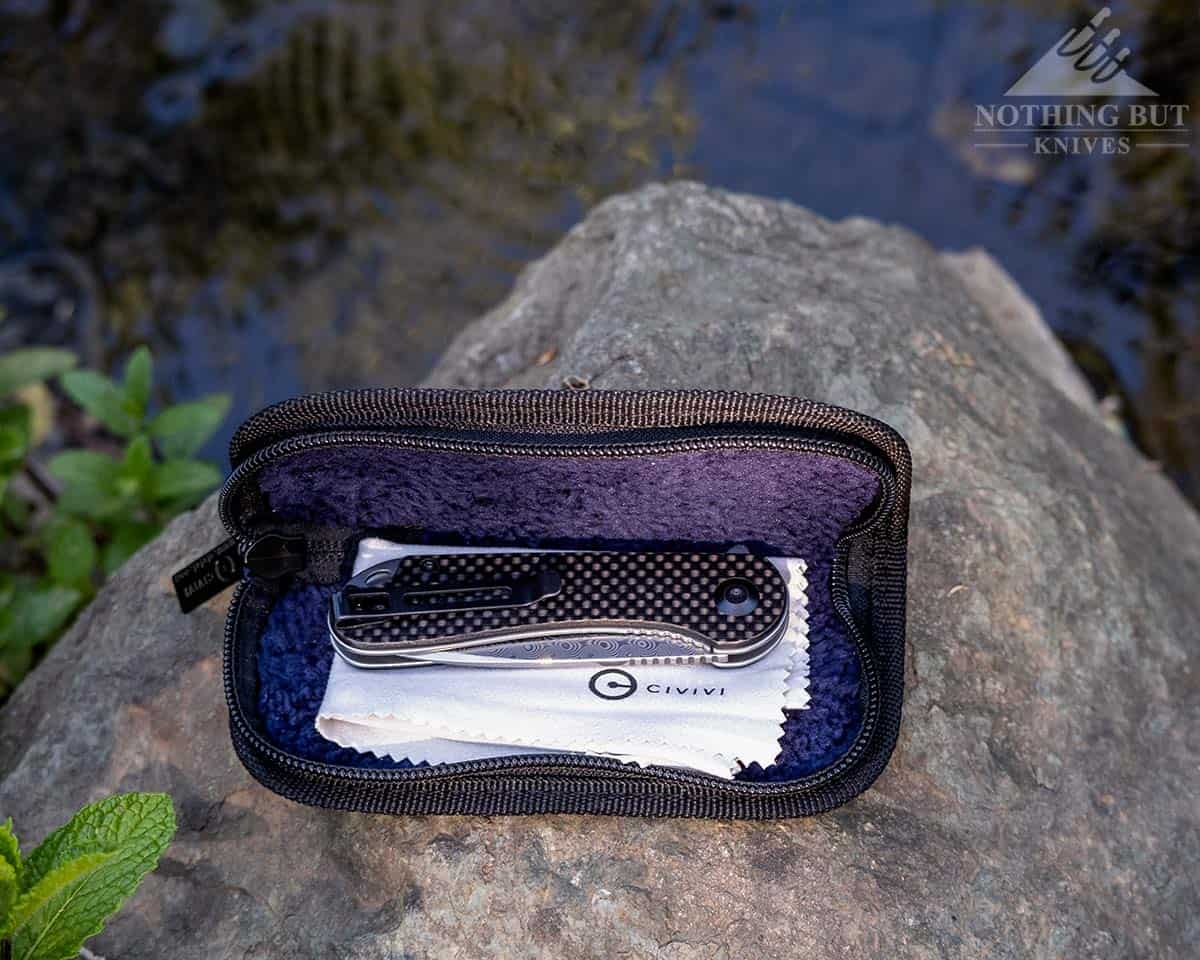The Civivi Elementum Damascus knife inside it's caes on a rock next to a creek. 