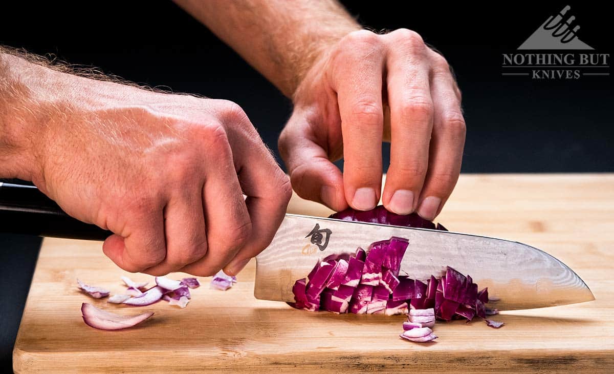 A close-up of the Shun Classic santoku knife dicing a large red onion. 