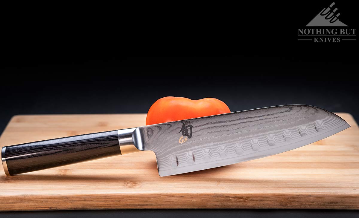 Header image for our Shun Santoku review featuring the knife with a tomato on a wood cutting board.