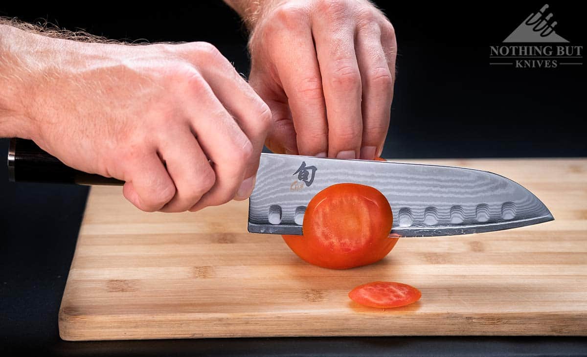A close-up of the Shun Classic Santoku knife cutting through a ripe red tomato.