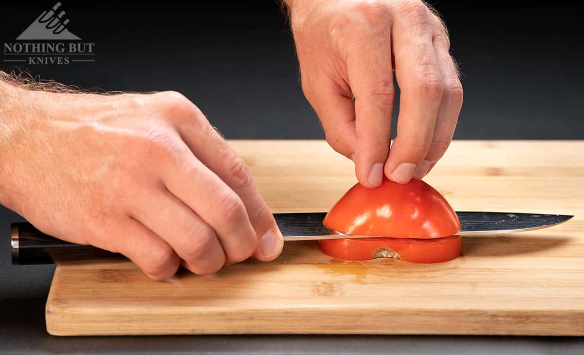 The Shun Classic Santoku slicing a tomato sidways on a wood cutting board. 