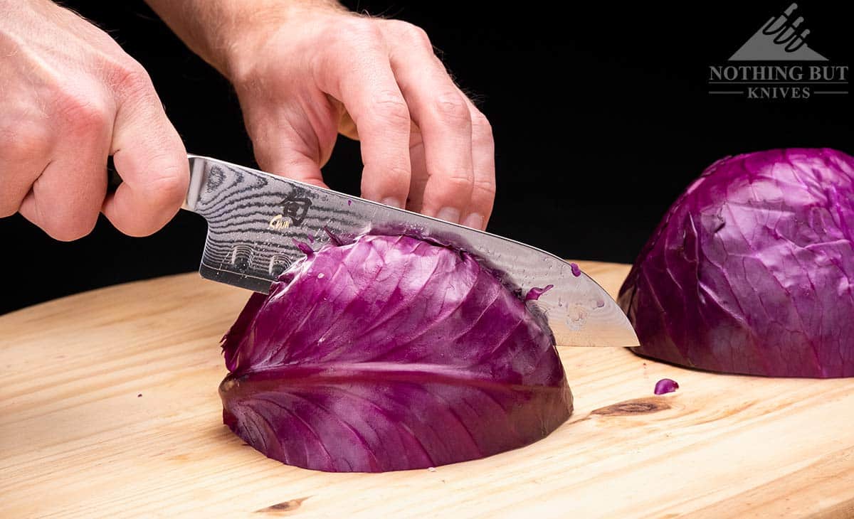 The Shun Classic Santoku slicing through a large red cabbage on a wood cutting board. 