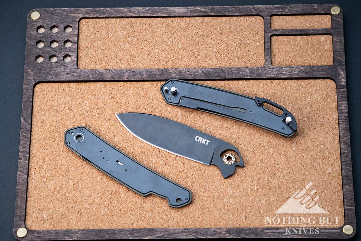The CRKT Bona Fide OD Green field stripped on an Asphalt Tray. Close-up showing the knife in three parts.