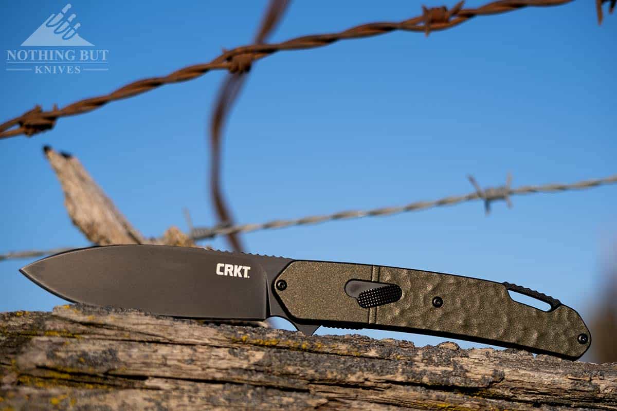 The Bona Fide OD Green pocket knife in the open position on a barbed wire fence.