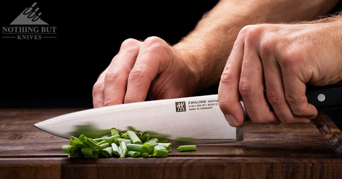 The Professional S Chef knife chopping green onions on a wood cutting board. 