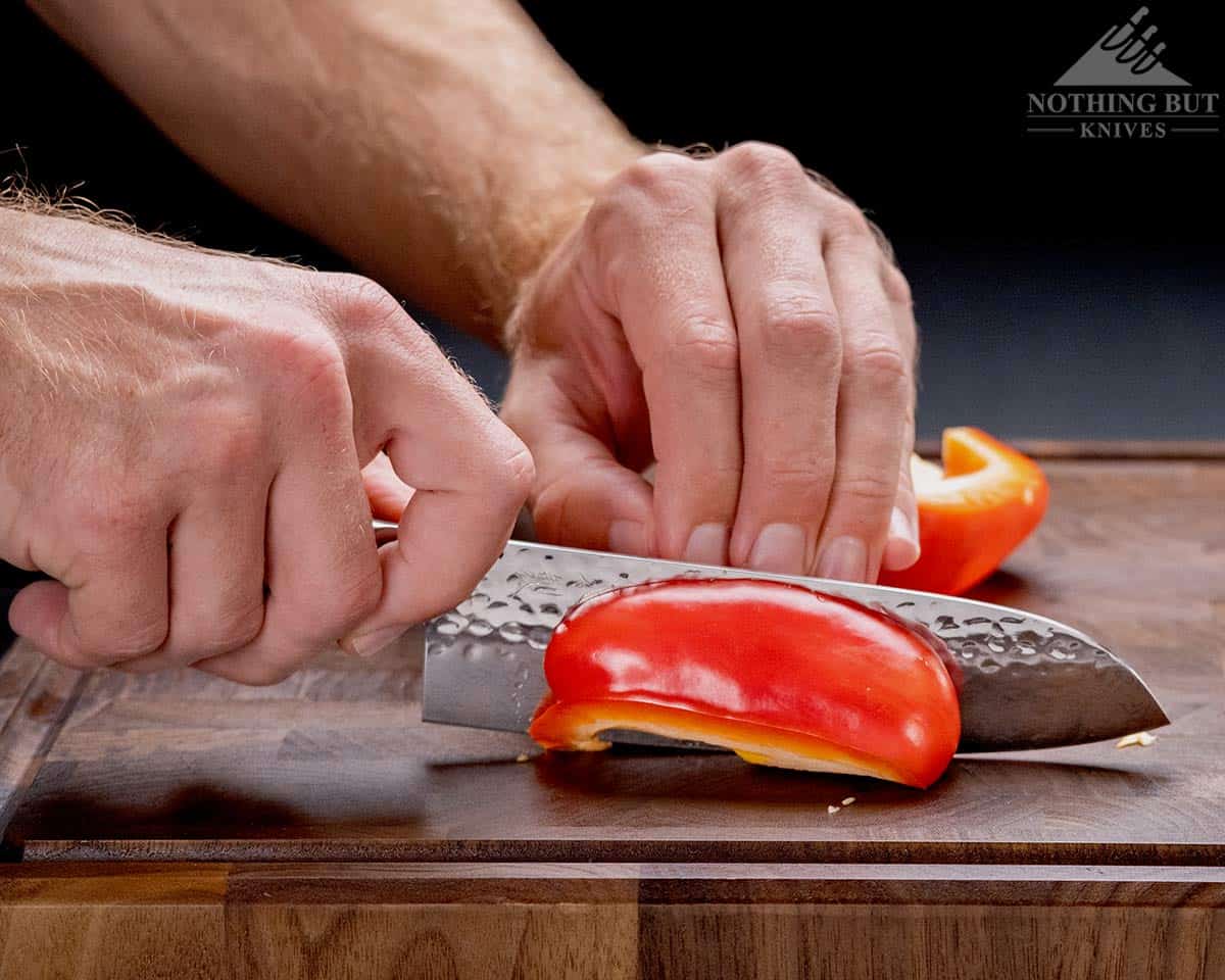 A close up of an Enso Santoku knife in a person's hand slicing up a red bell pepper. 
