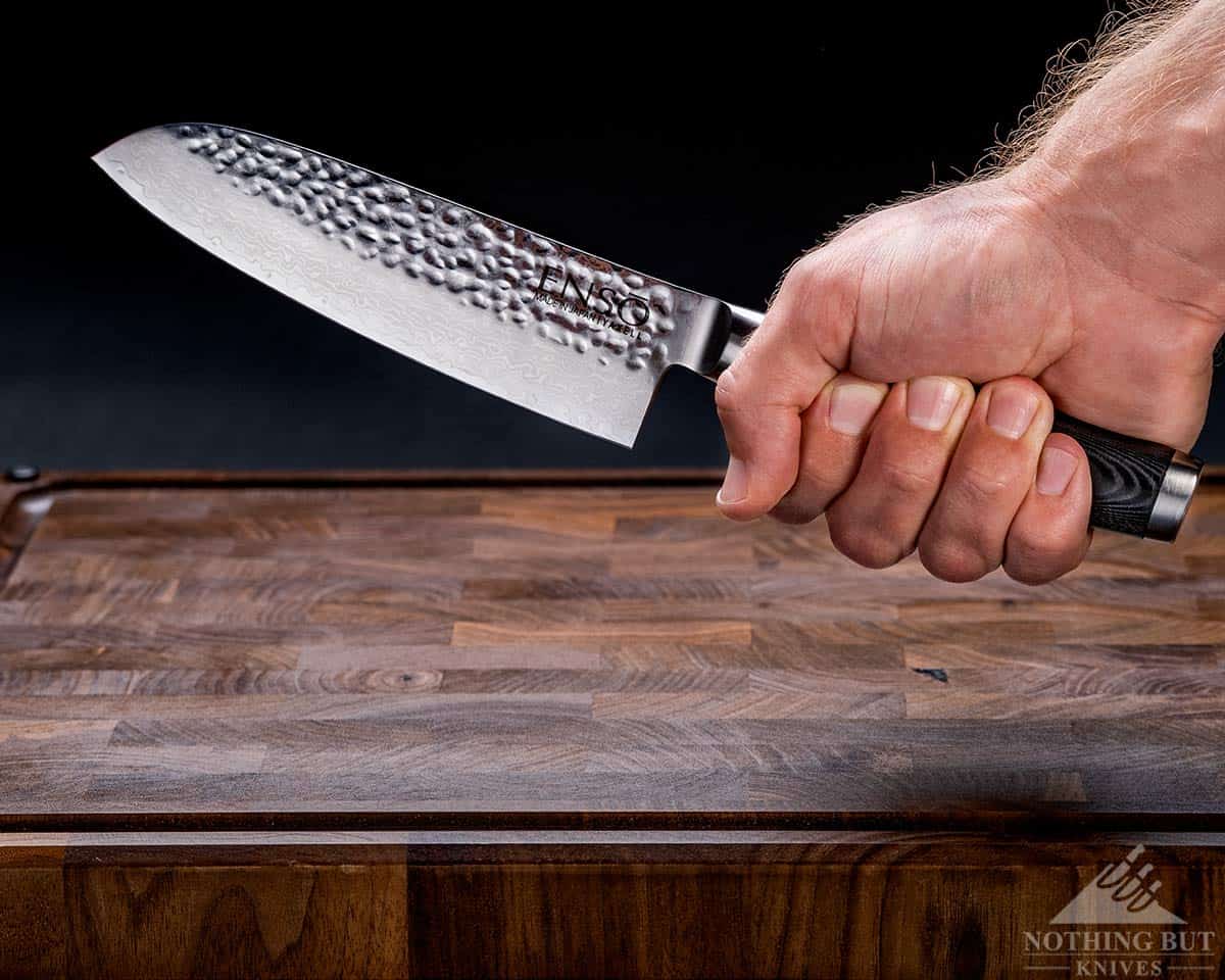 A close-up of a man's hand gripping the handle of the Enso HD Santoku knife in front of a black background. 