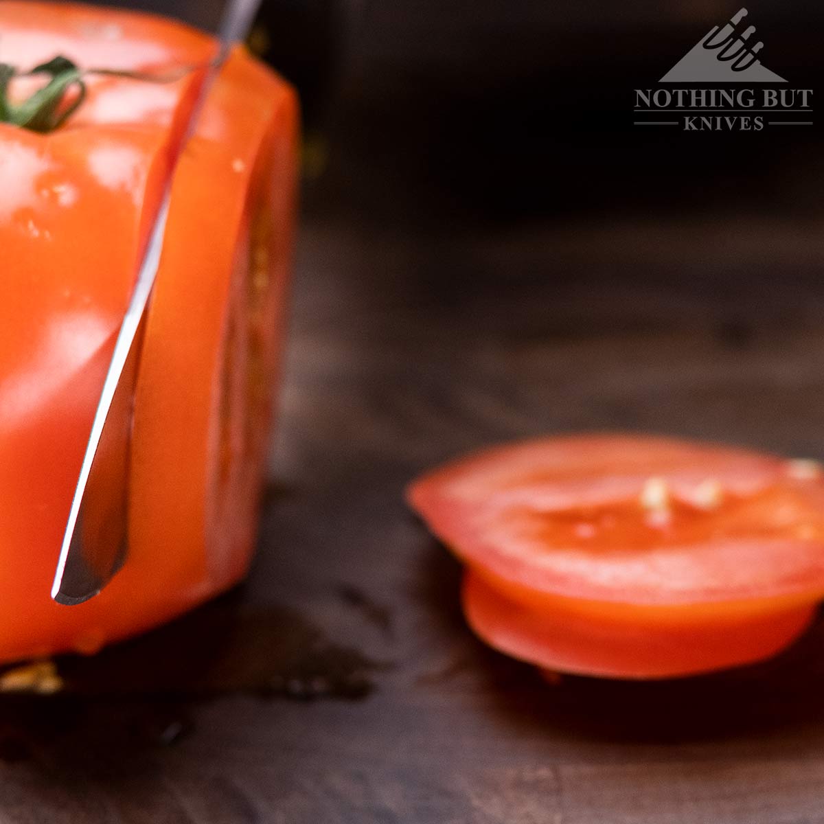 Close-up of a chef knife tip half way through a cut on a tomato. 