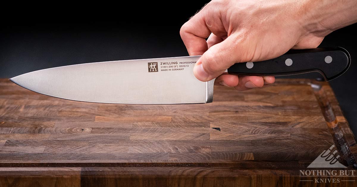 Zwilling 8 Inch Professional S Chef Knife Review - Image 10 A close-up of a man's hand holding the Zwilling Professional S Chef knife in a pinch grip above a wood cutting board.