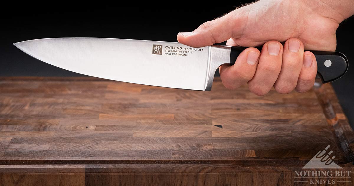 A close-up of a man's hand holding the Professional S chef knife in a Filipino grip above an end grain cutting board. 