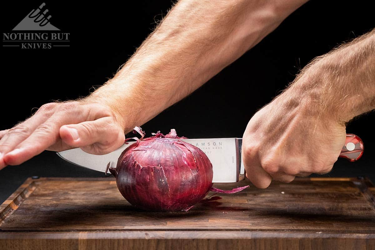 A close-up of an onion being split in two by a chef knife. 