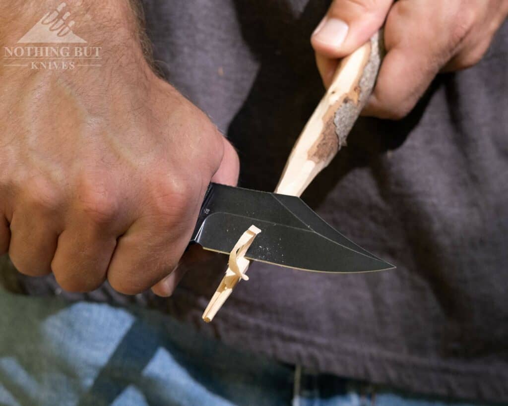 A close-up of a man's hands carving a stick with the Off-Grid Caiman as part of our in depth knife review. 