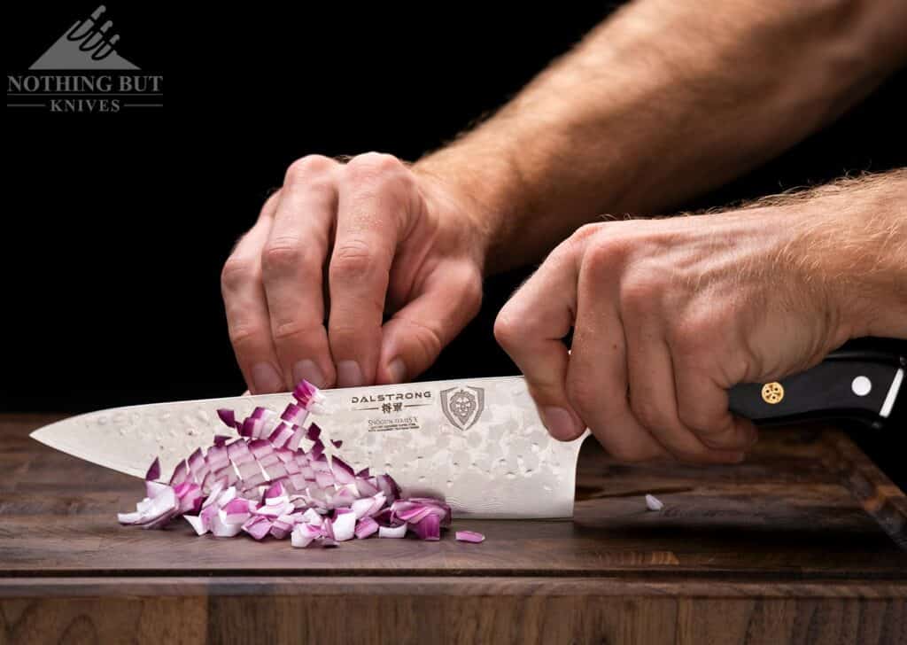 A close-up of the Shogun X series chef knife chopping a red onion of an end grain cutting board. 