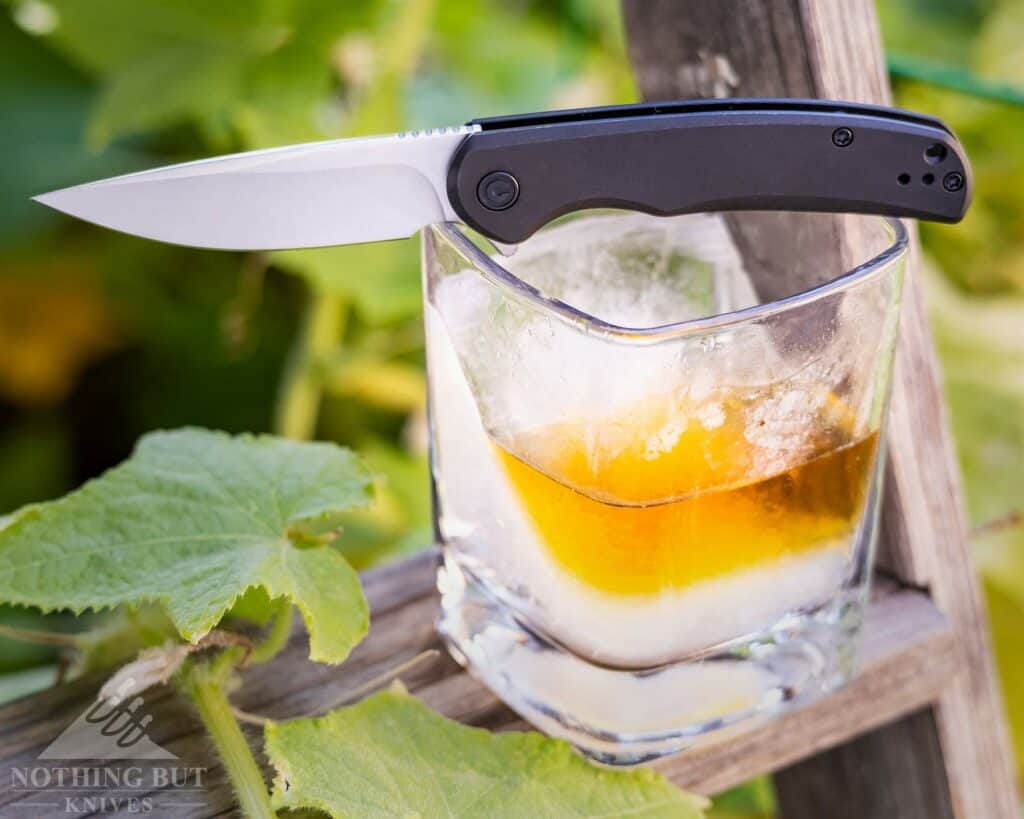 Folding knife sitting on a glass of bourbon outdoors. 