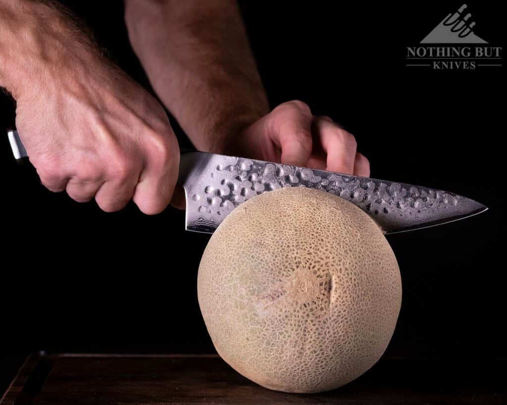 A close-up of a person's hand slicing through a cantaloupe with the Shogun Chef knife.