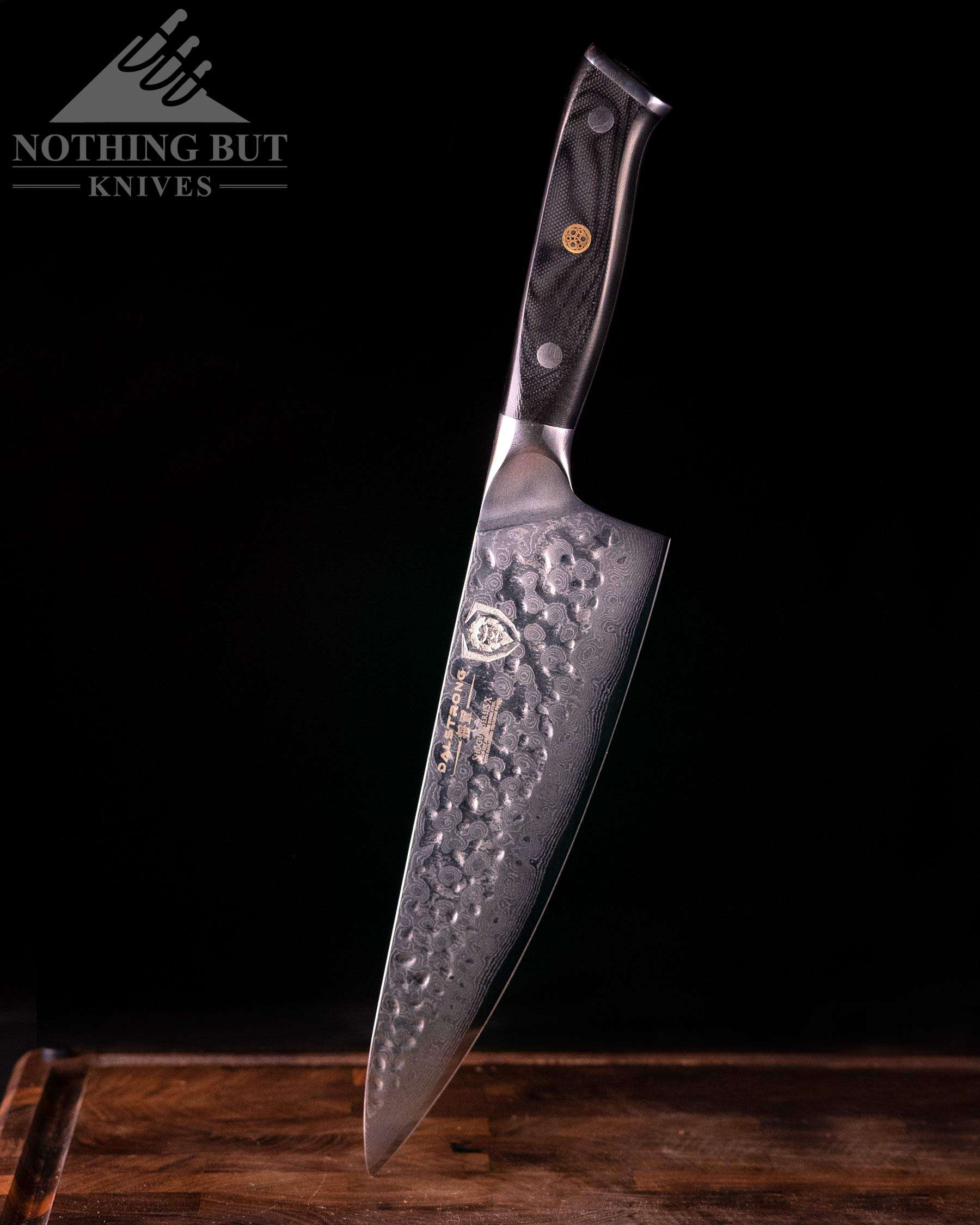 The Dalstrong Shogun Series X Chef Knife with its tip down on a wood cutting board and its handle in the air showing the branded side of the blade.