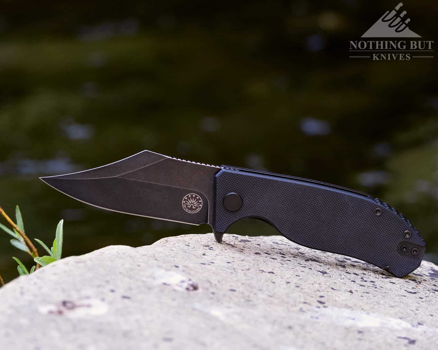 We reviewed the Off-Grid Caiman Bowie style folding knife. It is pictured here on a granite rock in a mountain creek.