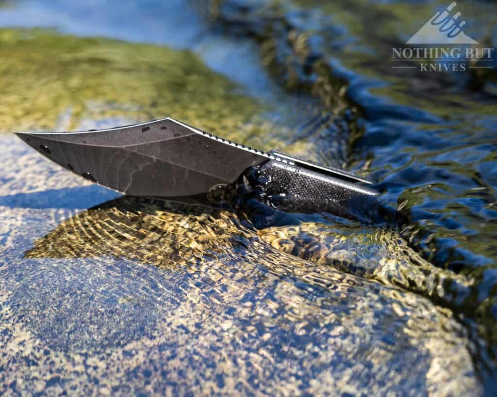 The Caiman pocket knife sitting in a creek partially submerged. 