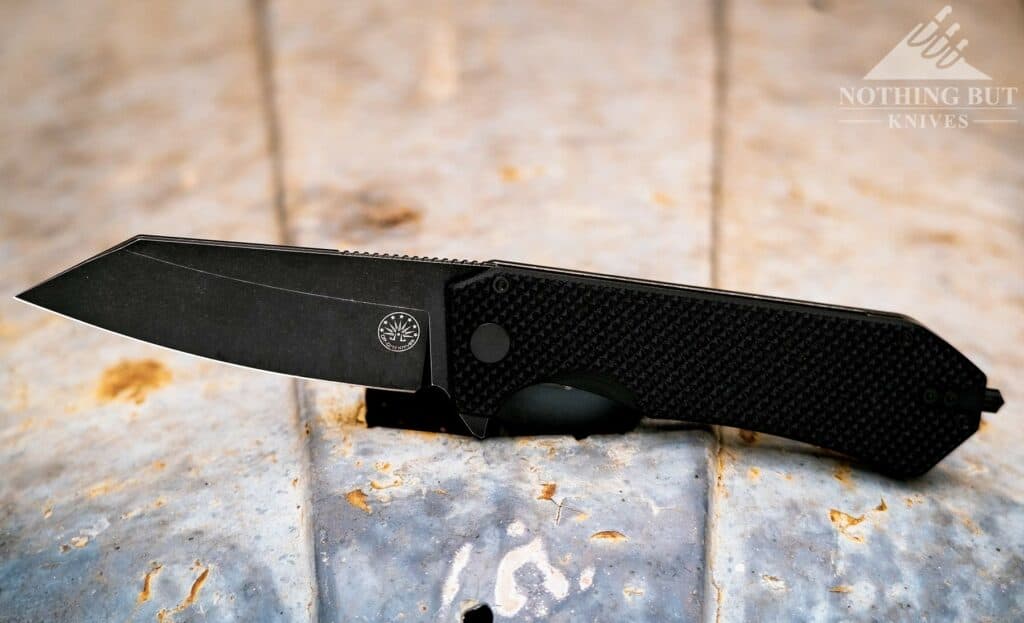 The Off-Grid Enforcer XL tactical knife in the open position of the hood of a rusty tractor hood. 