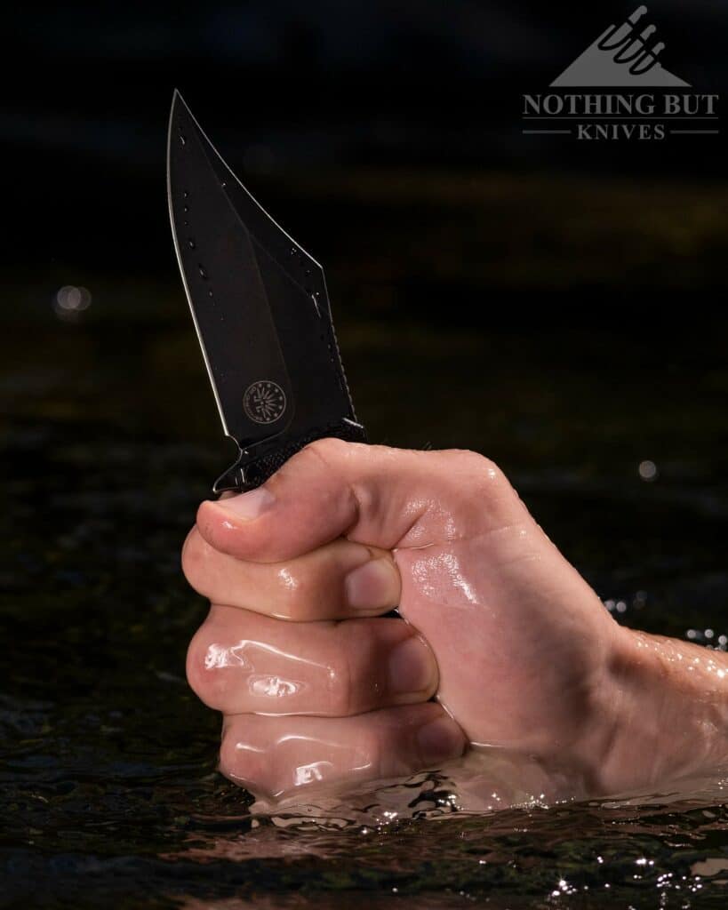 The Off-Grid Caiman Bowie style pocket knife being held out of the water in a man's hand. 