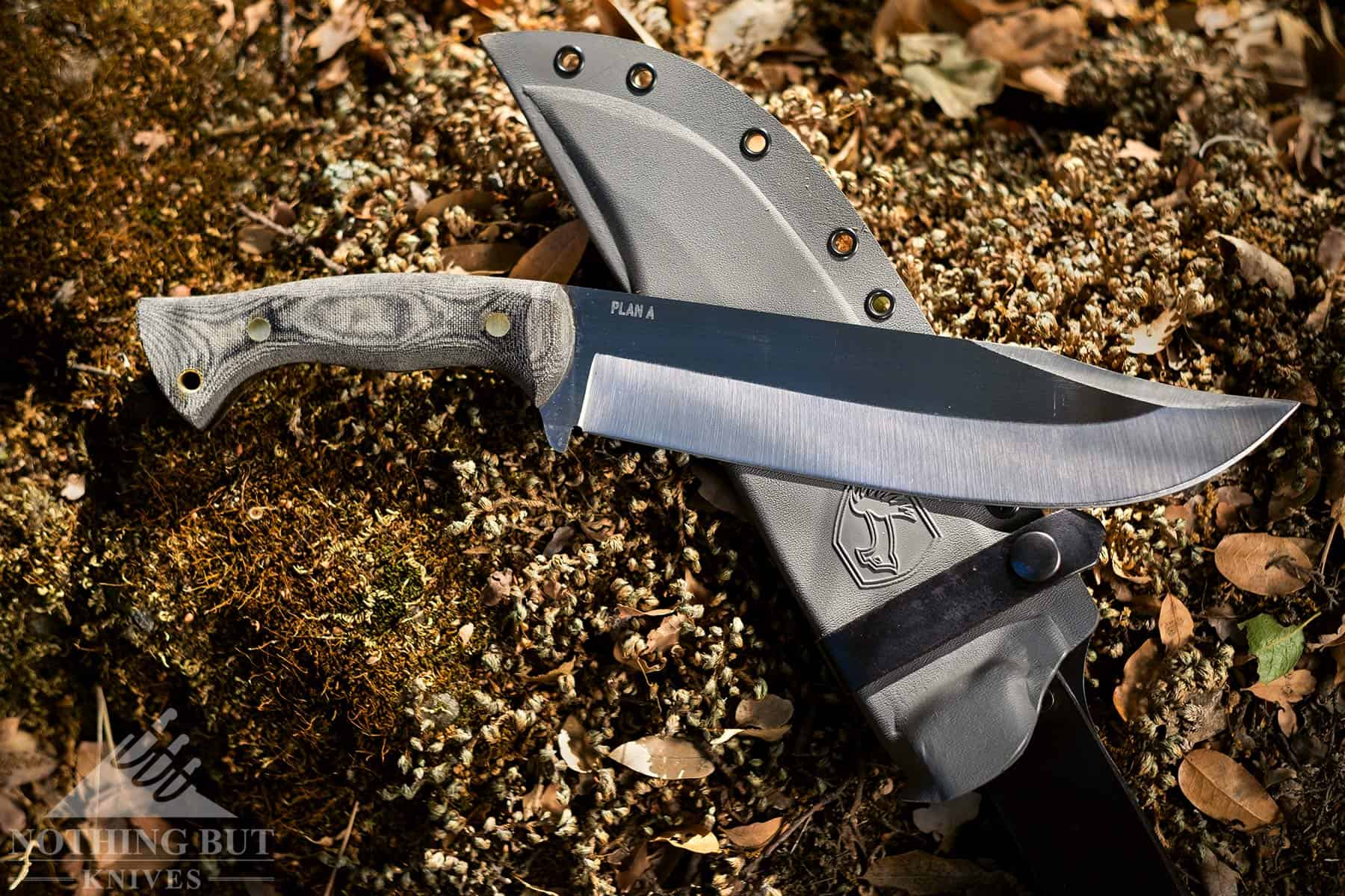 The Condor Plan A Bowie shown here with it's kydex sheath on a mossy rock outdoors.