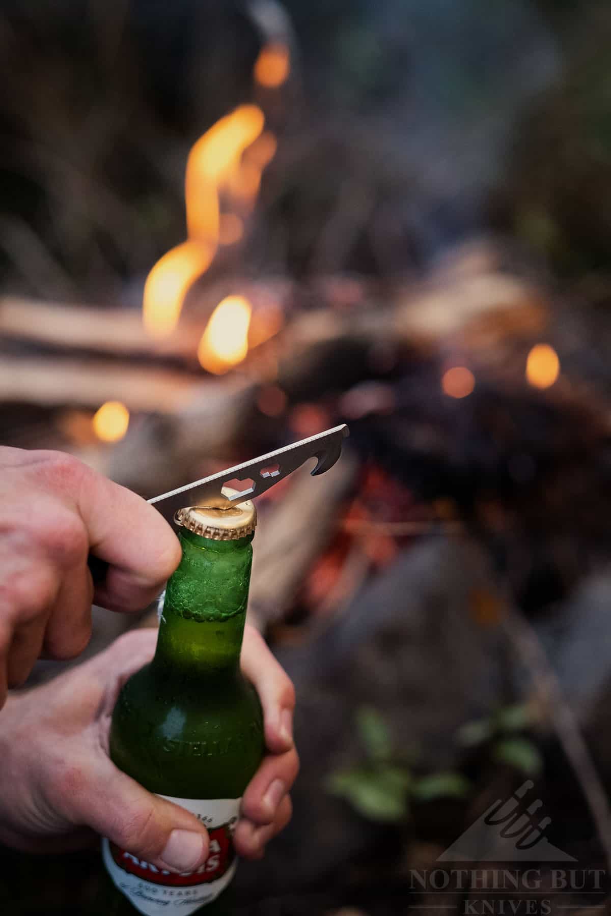 Civivi Crit Knife Review - Image 11 A beer bottle being opened with the Crit's tool bar by a campfire. This illustrates our favorite use of the Civivi Crit in this review.