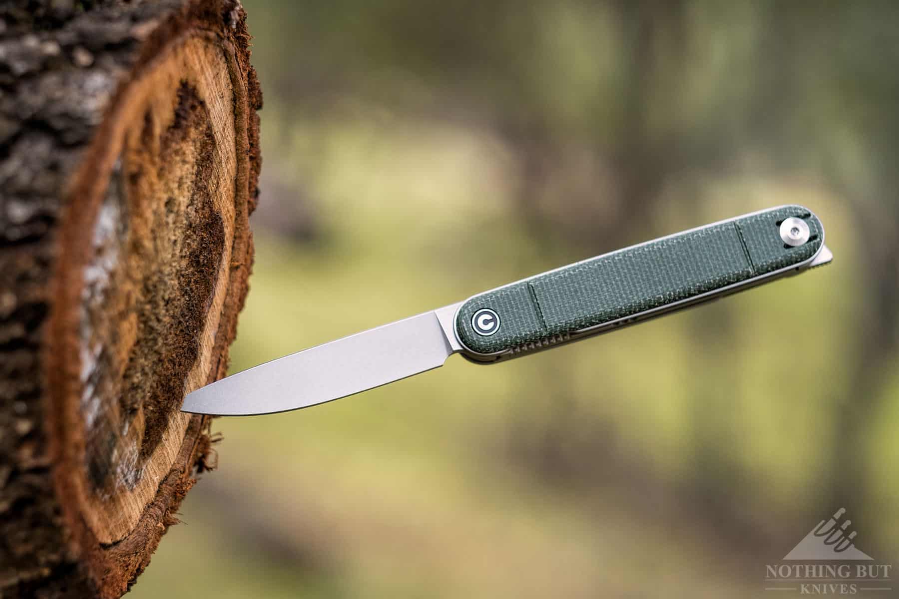A close-up of the Civivi Crit pocket knife sticking out of a tree stump.