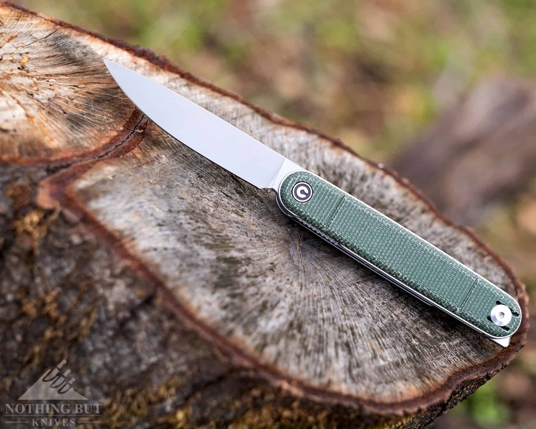 The Civivi Crit folding knife with one blade open on a tree stump.