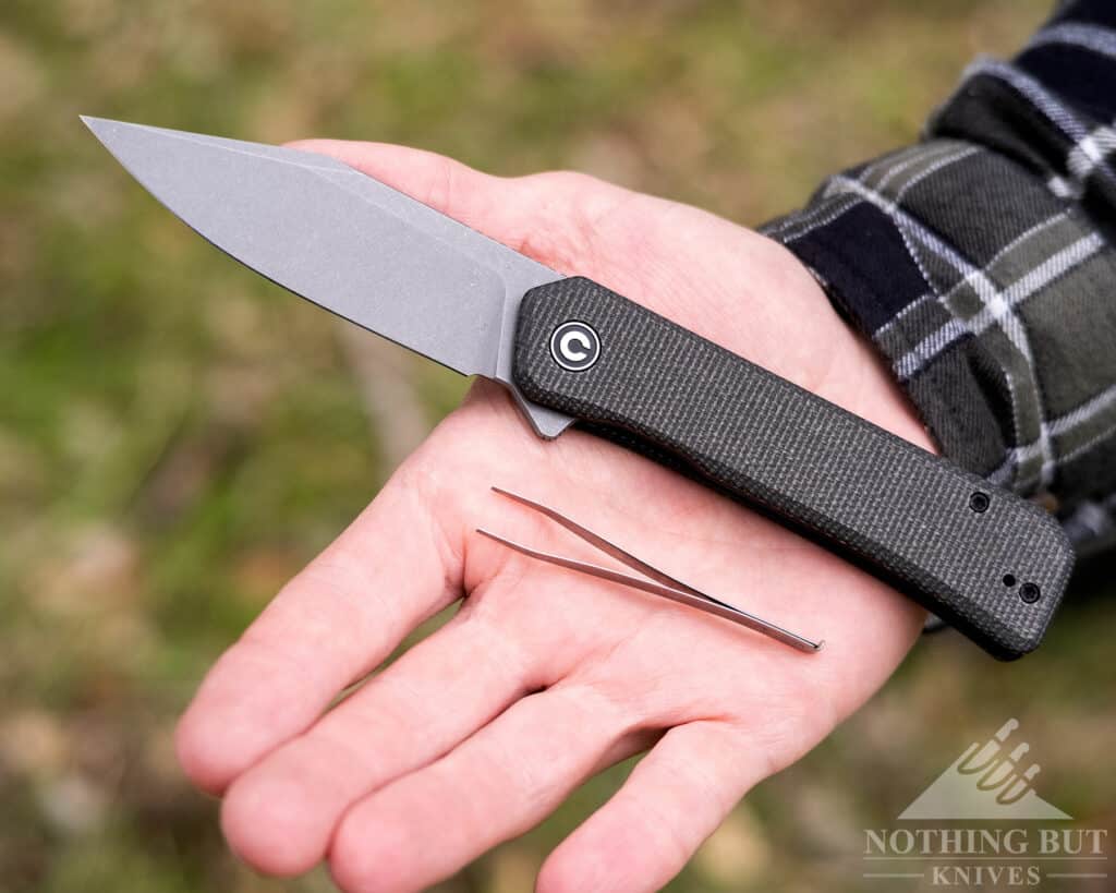 The CIvivi Relic pocket knife shown here in a man's hand for scale with the included pair of tweezers. 