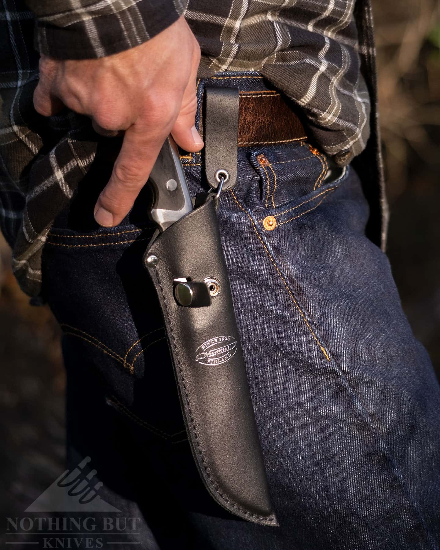 Marttiini Full Tang Review - Image 10 A person drawing the Marttiini Full Tang from it's black leather sheath.