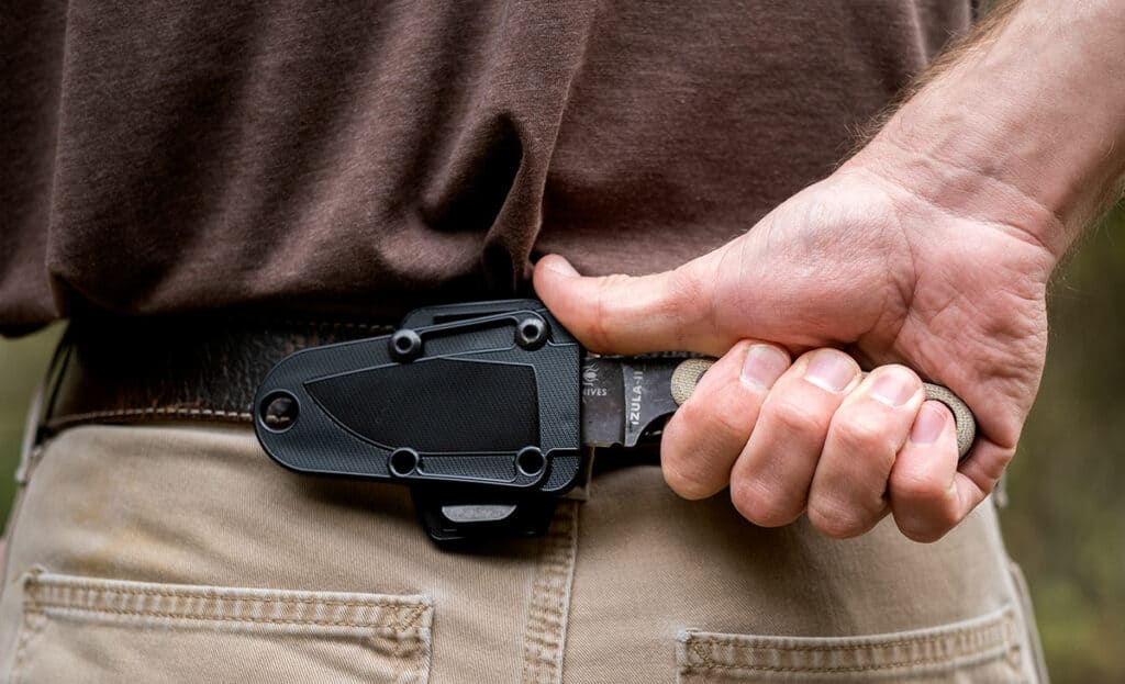 The Esee Izula 2 shown in the scout horizontal carry position on a person's back to show scale. 