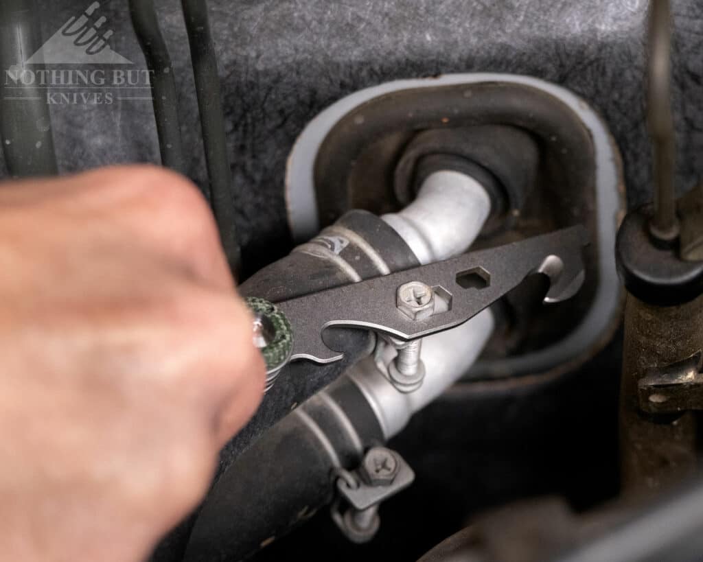 A close-up of the Civivi Crit tool bar being used to tighten a bolt on a car vacuum tube.