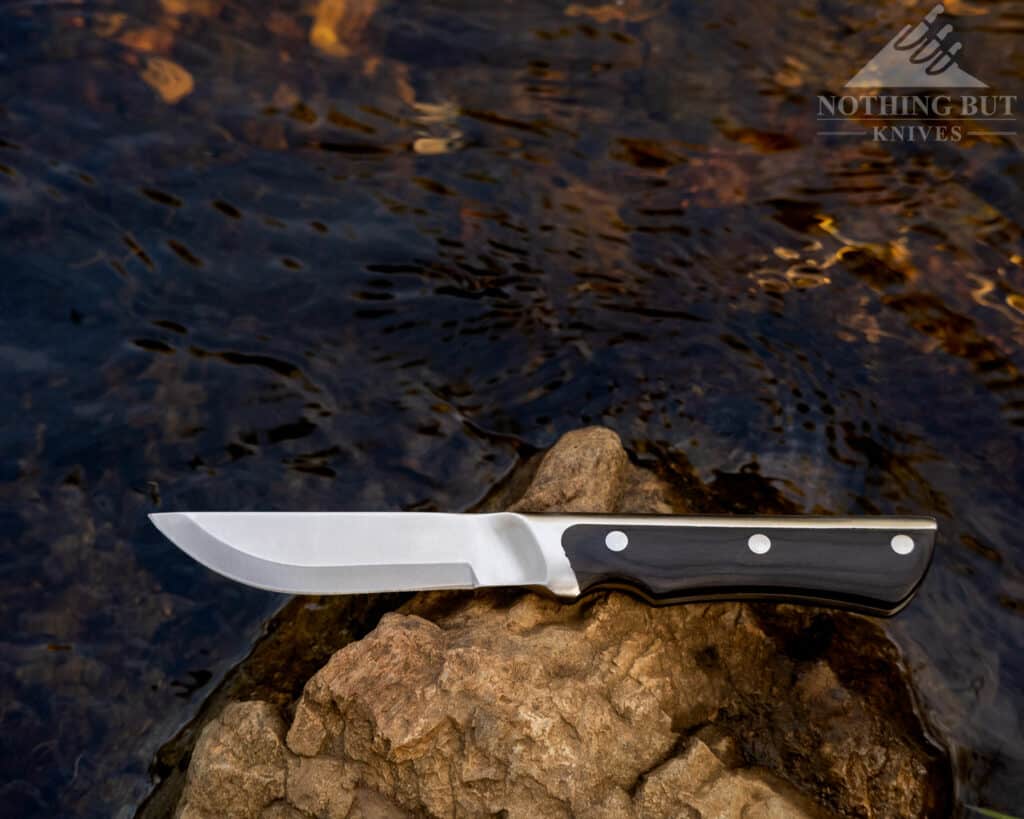 Shot of the Marttiini Full Tang knife next to a mountain creek. This image shows the handles and the scandi grind blade. 