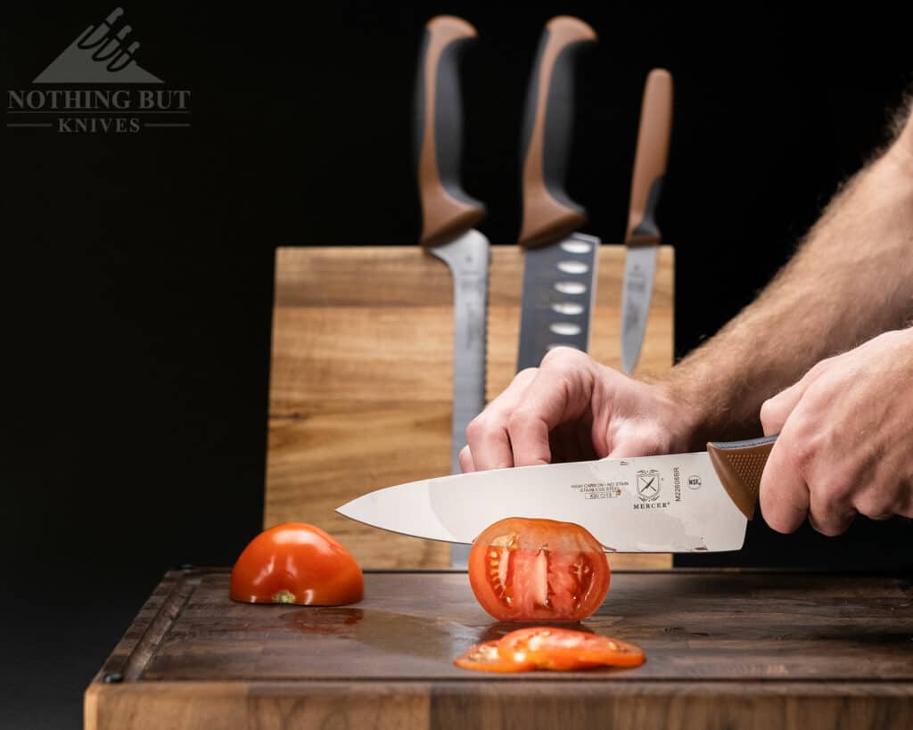 The Mercer Culinary Millenia chef knife with a chocolate handle easily slicing through a tomato. This image shows the ability of the chef knife included in this set. 