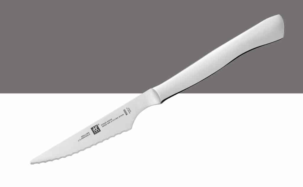 A single Zwilling Stainless Steel Serrated steak knife on a gray and white background. 