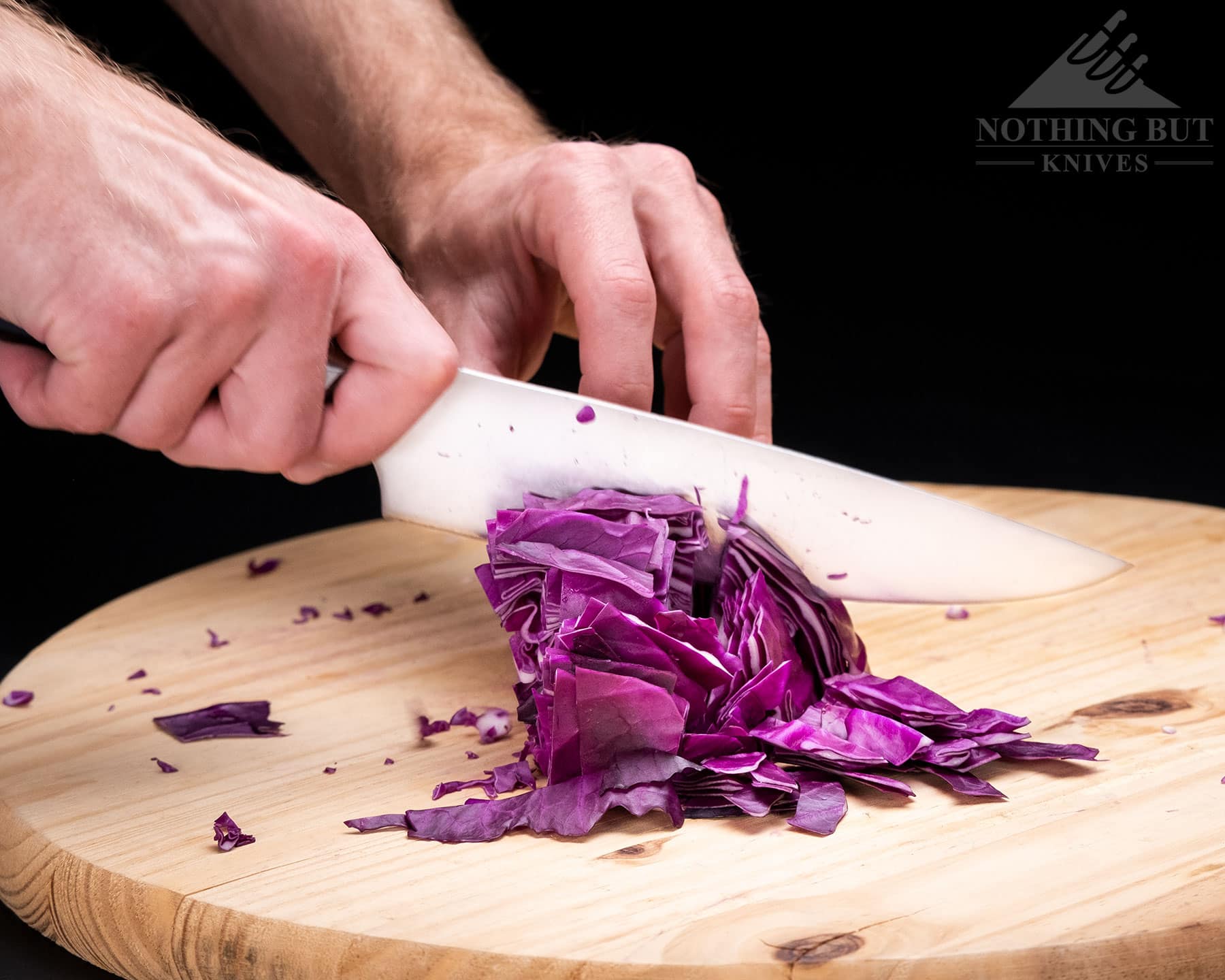 The 8 inch Cangshan TC chef knife chopping a red cabbage on a wood cutting board. 