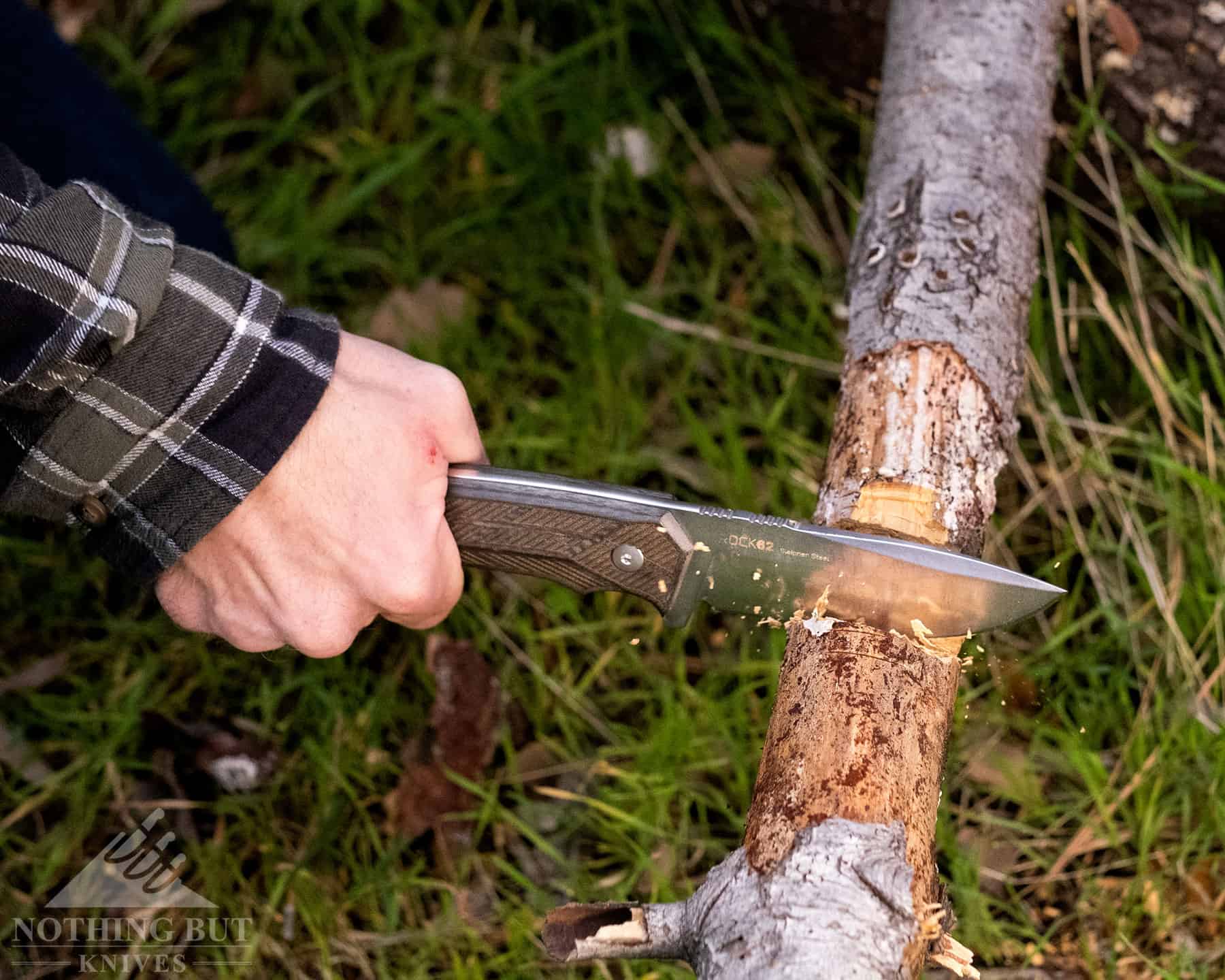 A Woox fixed blade knife shown chopping through a tree branch. 