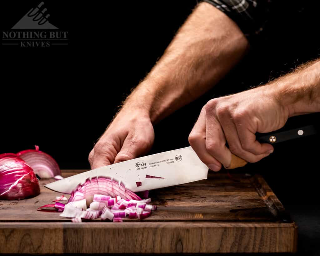 A persons' hand holding the Cangshan TC chef knife and chopping a red onion. 