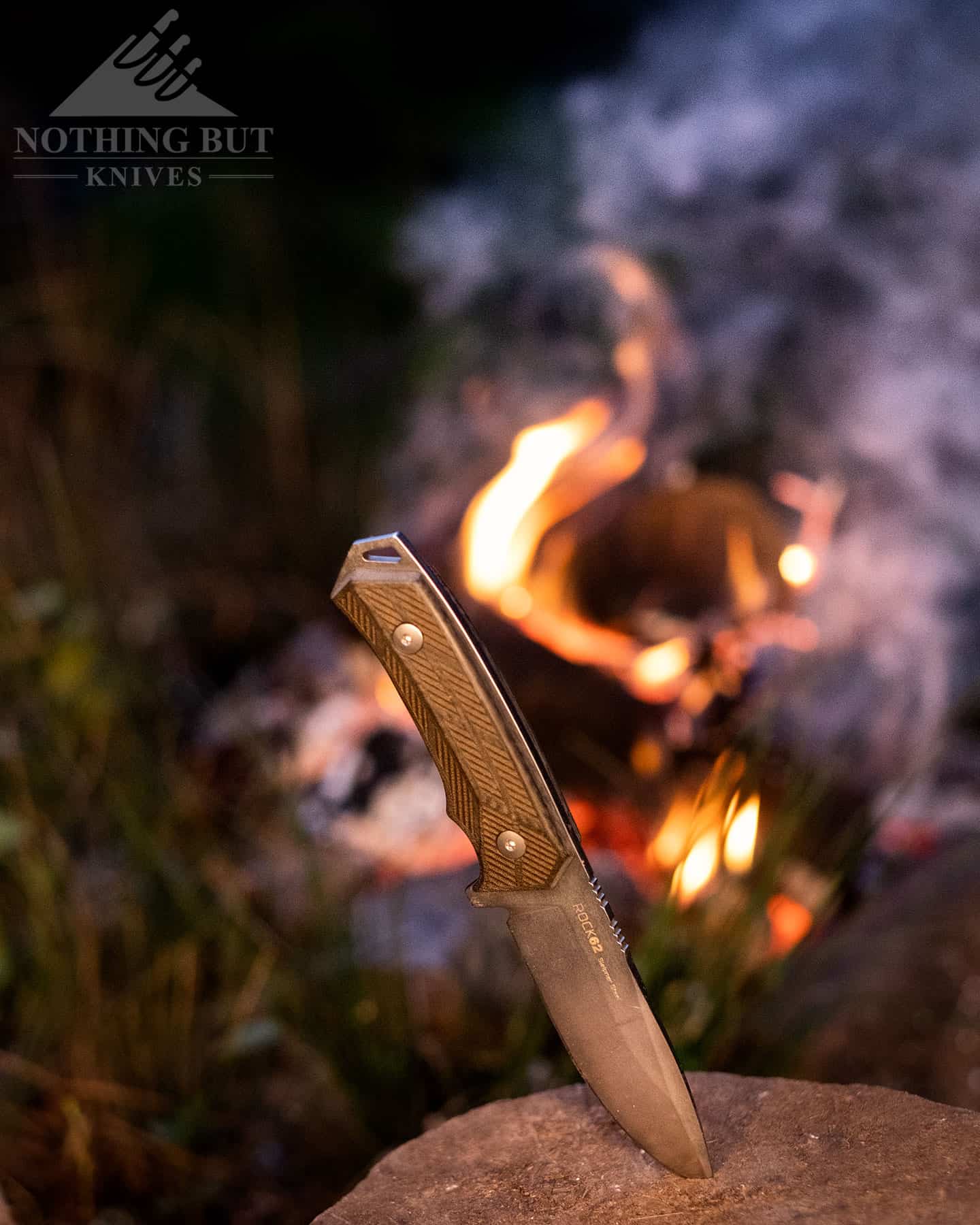 The Woox Rock 62 camping survival knife shown stuck in a chunk of wood next to a camp fire.