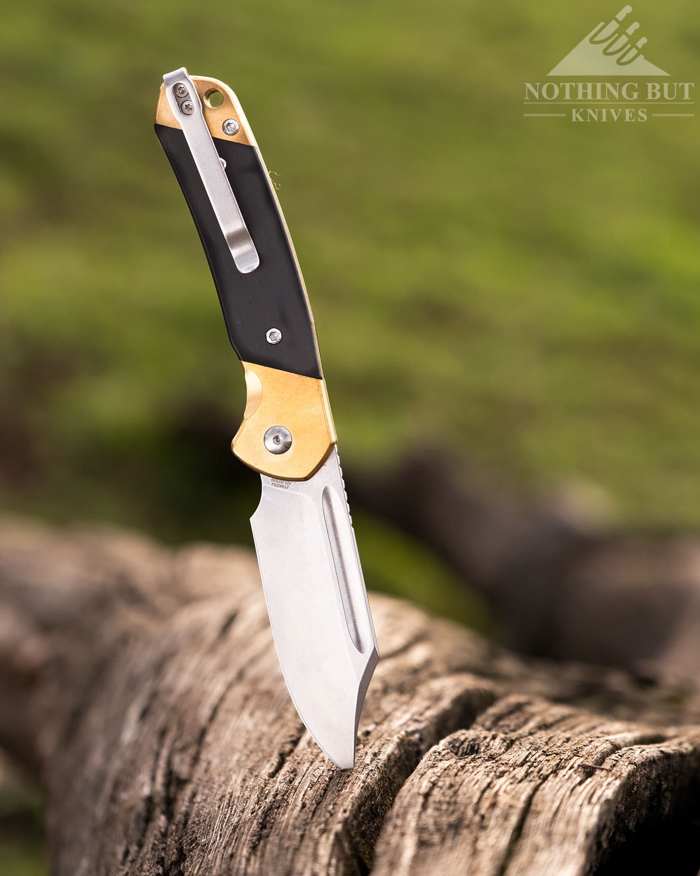 Best Slip Joint Knives For Nostalgic Edc - Image 8 The CJRB Pyrite shown here with the blade in the open position sticking out of a dead log in a green field.