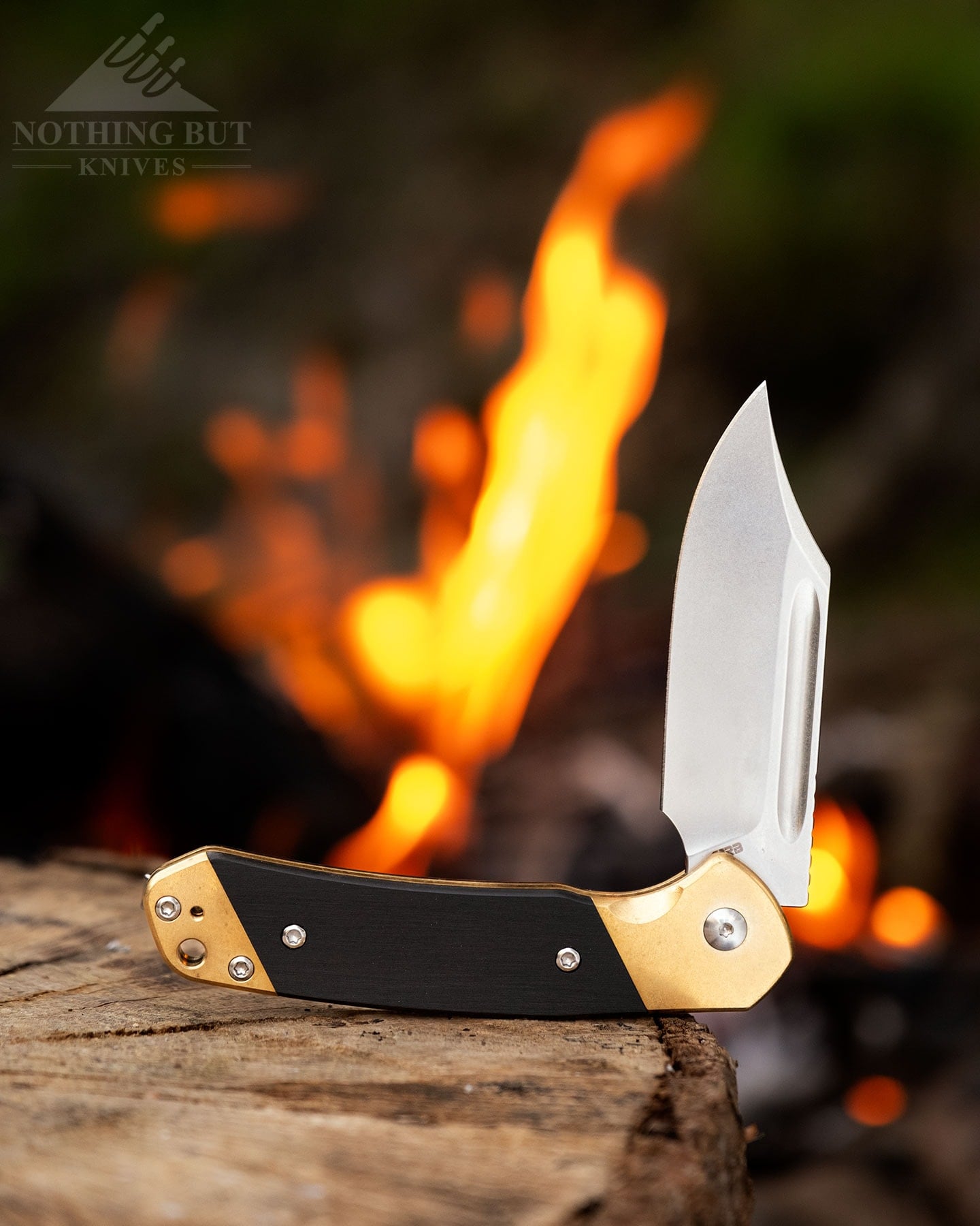 Best Slip Joint Knives For Nostalgic Edc - Image 10 A slip joint knife with a Bowie style blade in the half open position on top of a log in front of a campfire.