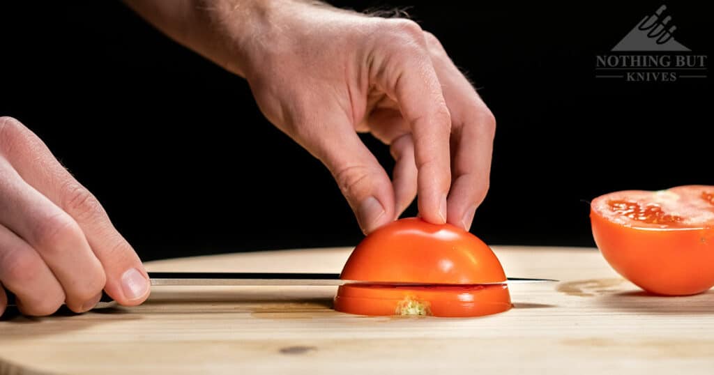 The Cold Steel Kitchen Classics Chef Knife slicing easily through a tomato to show the readers it's ability to cut through a tomato without smooshing it. .