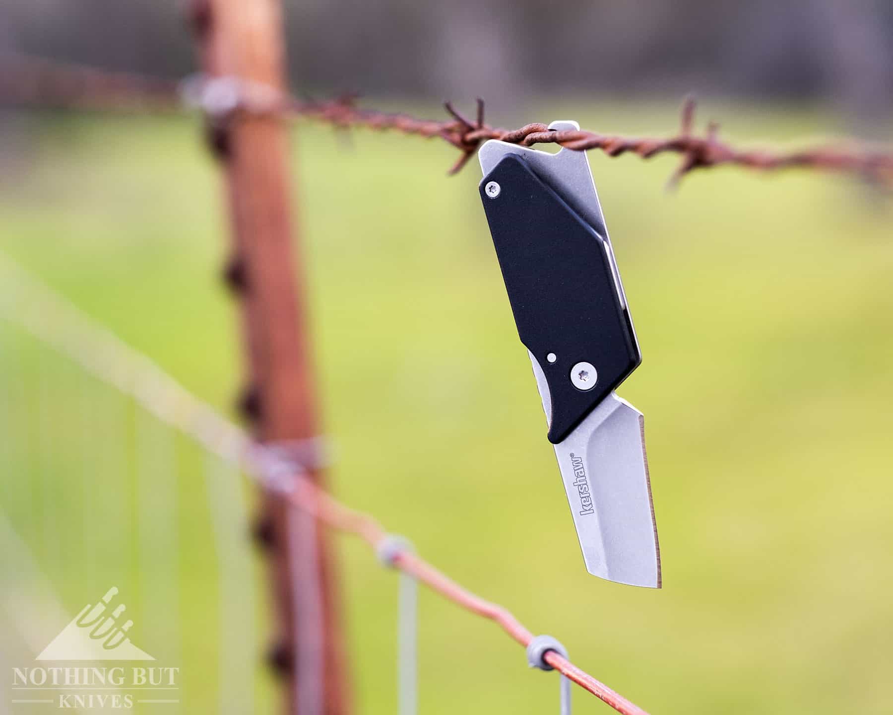 The Kershaw Pub has a bottle opener on the back of the tang. It is shown here hanging from a barbed wire fence. 