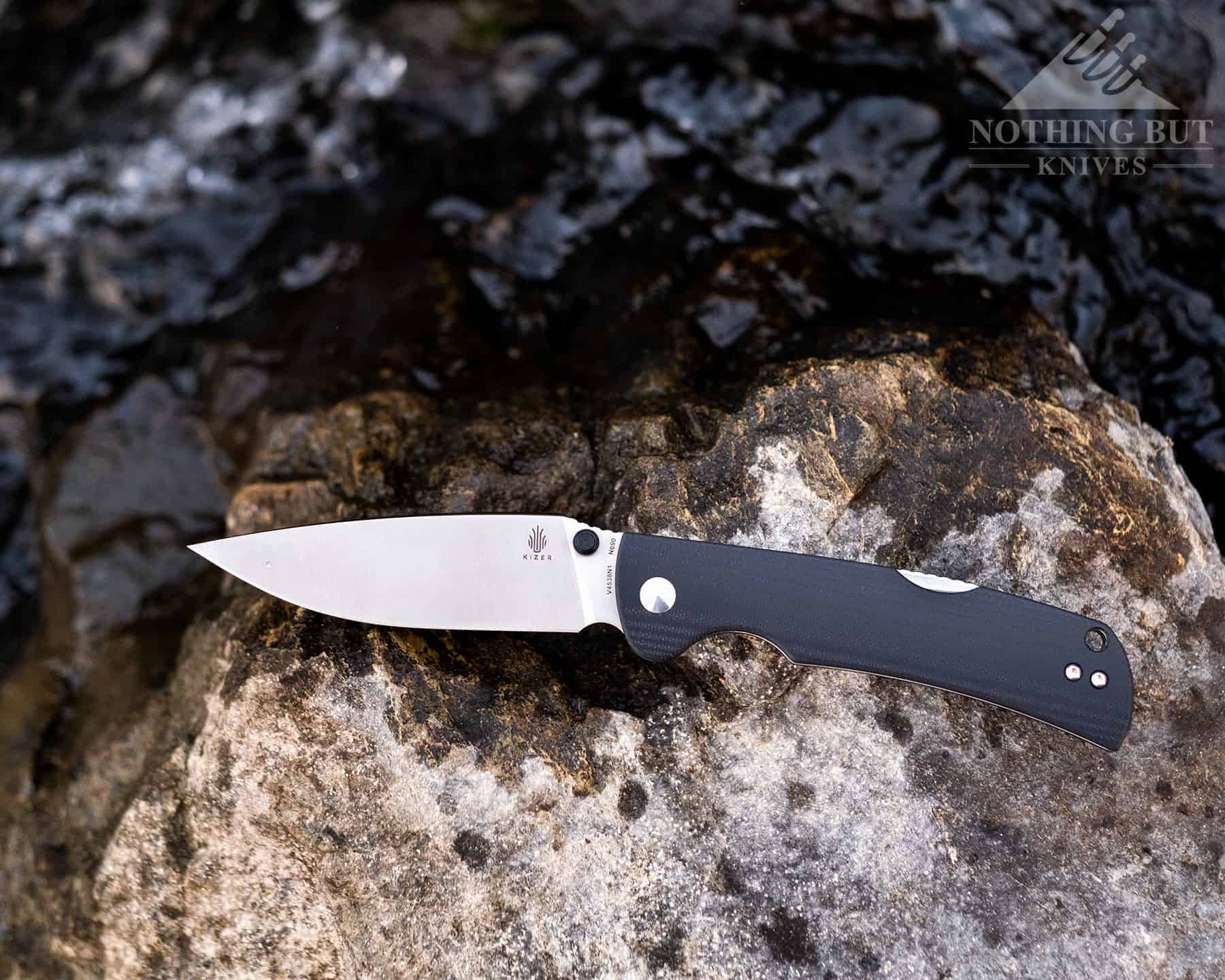 The Kizer Slicer Lockback folding knife is a great hard use knife with a strong lock. It is shown here on a rock next to a creek. 