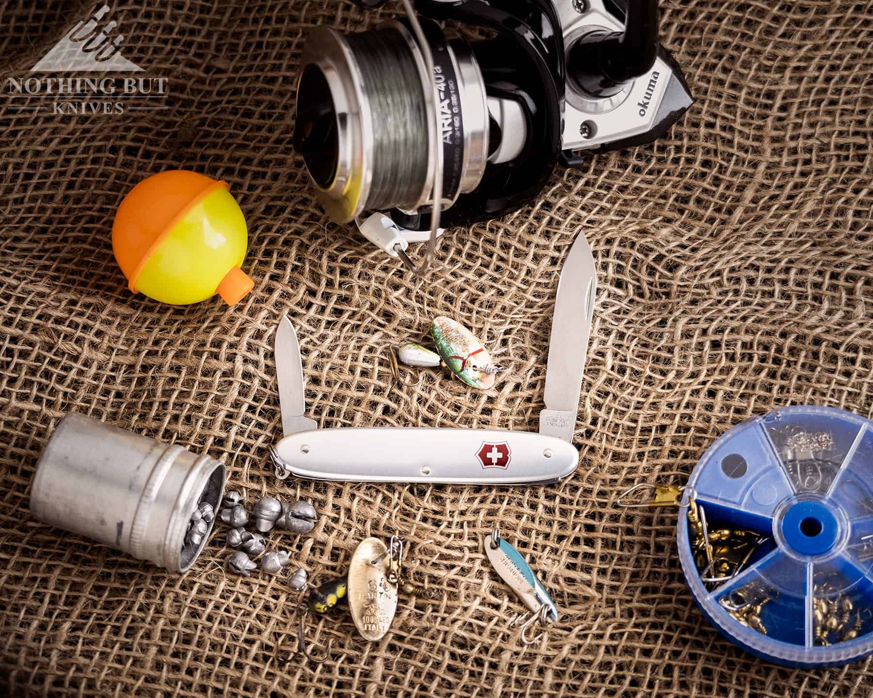 The Victorinox Secretary slip joint pocket knife makes nice addition to a fishing kit. It is shown here with fishing gear on a burlap background.  