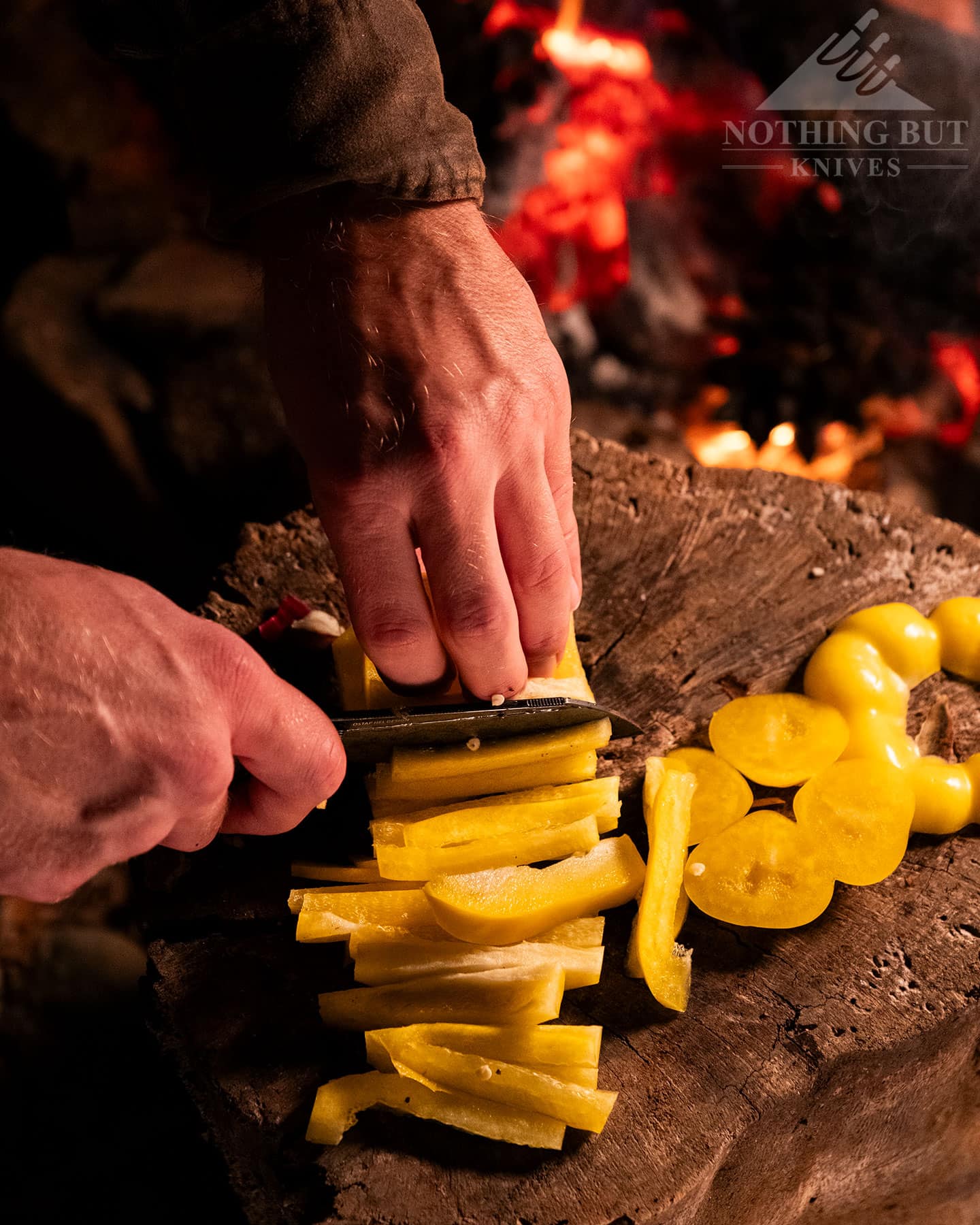 Our Search For The Best Camping Chef Knife - Image 10 An overhead view of the Civivi Hid camp cooking knife being used to slice a yellow bell pepper on a tree stump next to a campfire in the Sierra Nevada Mountains of Northern California.