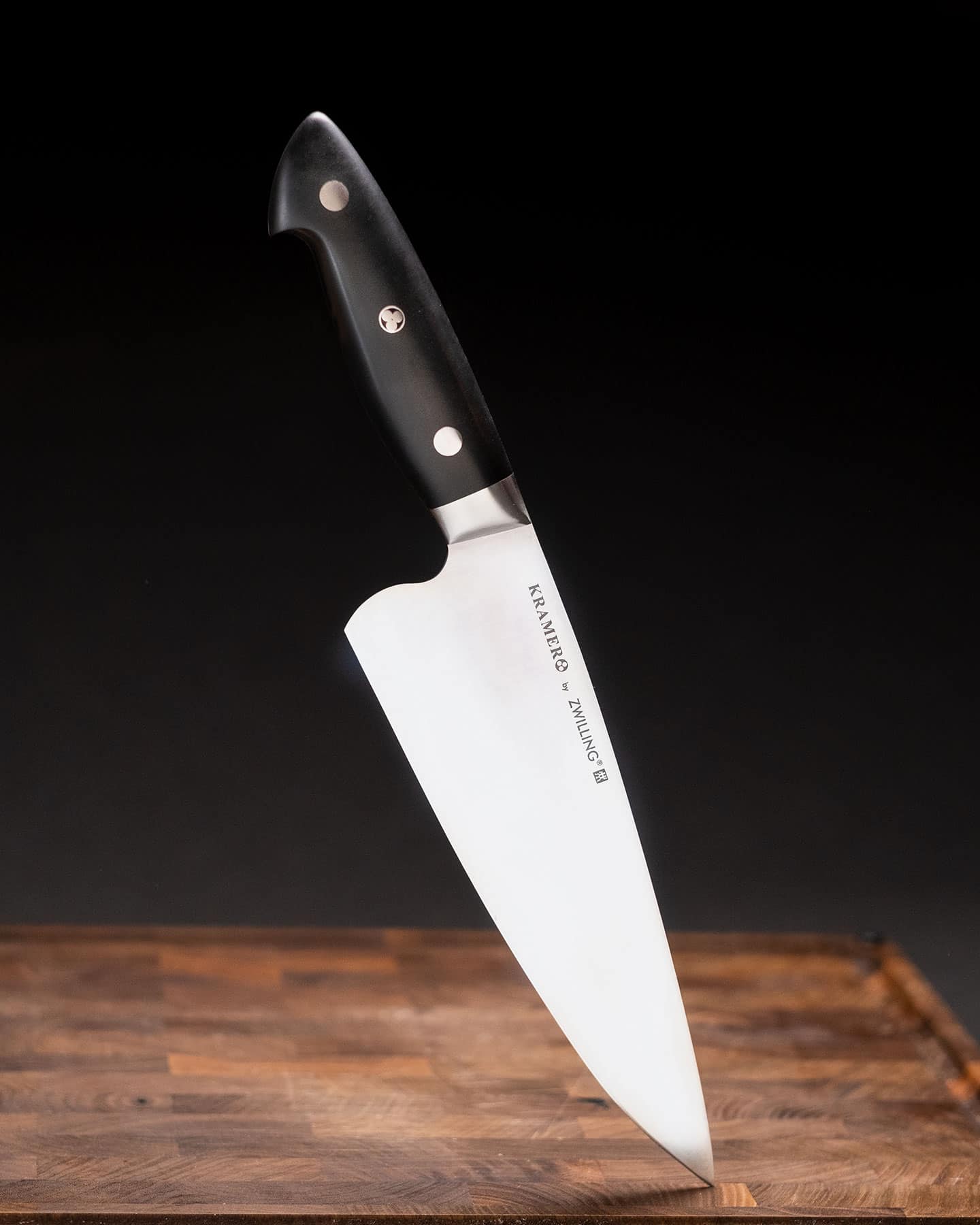 Cangshan Thomas Keller Chef'S Knife Review - Image 7 Header image for our in-depth review of the Kramer By Zwilling Euro Essential Chef Knife Review featuring the knife on a wood cutting board in front of a dark background.